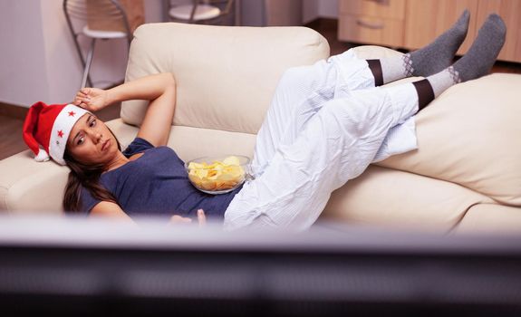 Adult person relaxing on sofa changing channel using remote searching xmas movie