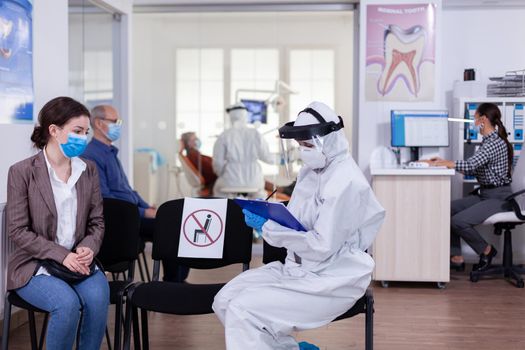 Dentist assistant with ppe equipment talking with patient
