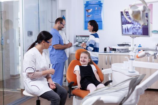 Dentist in dental office making little girl laugh Child with her mother during teeth check up with stomatolog sitting on chair.