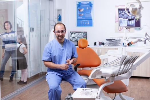 Professional dentist discussing about multiple teeth hygine issuees sitting on chair. Stomatolog in professioanl teeth clinic smiling wearing uniform looking at camera.