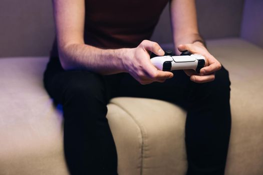Males hands holding joystick, playing video game and having fun. Close-up of the man holding a white joystick next gen console and playing a video game on TV
