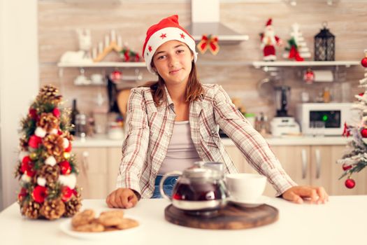 Joyful girl wearing santa heat celebrating christmas in kitchen