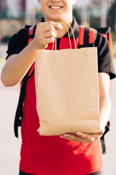 Happy delivery worker holding packet with food looking at the camera and smiling. Close up portrait of positive young man courier person. Delivery service door to door