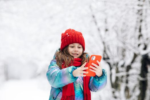Cute little girl taking a selfie in the winter forest. Winter travel with children concept. Adorable happy smiling kid girl enjoy making selfie camera shot by smartphone