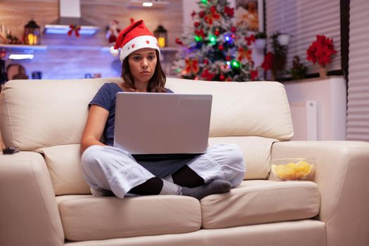 Woman writing business email on laptop sitting in lotus position on sofa
