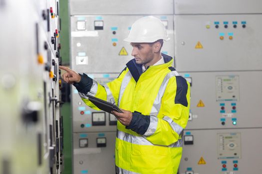Man electrical engineer hold tablet monitoring electrical system in control room. Technician inspect to control panel screen system for generate electricity of factory in manufacture industrial