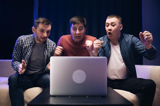 Male friends watching online football game match at laptop. Men fans buddies supporters cheering celebrating victory goal score support winning team. Men watching football in streaming on laptop