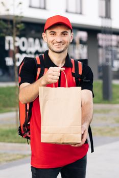 Food delivery man order from a restaurant. Handsome young man in a T-shirt and a cap. Happy delivery worker holding packet with food smiling. Delivery service door to door
