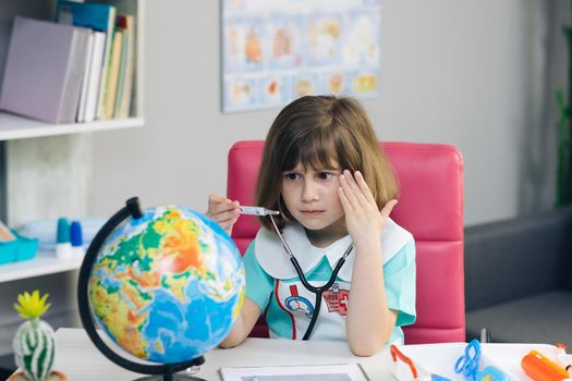Little kid girl dressed in a doctor's suit measures the temperature of the Earth. Ecology and global warming concept. Earth Temperature with Thermometer Icon for Global Warming and Climate Change.