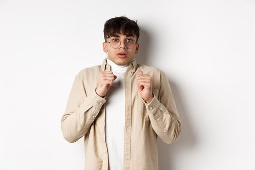 Startled man freeze from fear, gasping and looking scared at camera, standing in glasses on white background