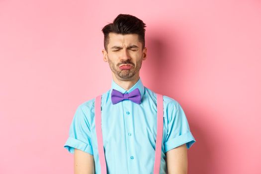 Sad and lonely man crying on valentines day, feeling lonely without lover, standing over pink background