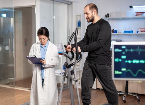 Sport researcher in laboratory taking notes while muscular athlete athlete is running