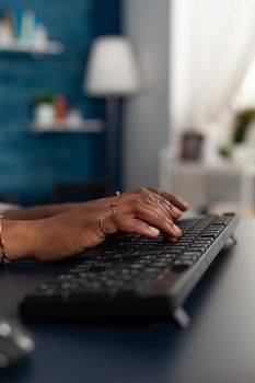 Closeup of black student hands typing education information on keyboard while working remote at business articole from home using computer. African american sitting at desk in living room
