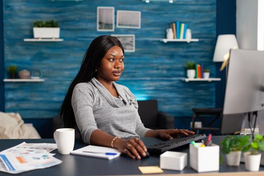African american student browsing communication information on computer during online courses working remote from home. Black woman sitting at desk in living room doing homework