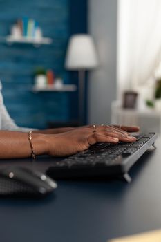 Closeup of black student working remote at education project typing information on keyboard using computer sitting at desk in living room. Woman searching business news article on internet