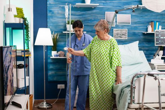 Support cargiver nurse helping retired senior woman caring intravenous drip bag