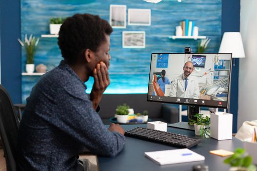 Healthcare consultation of african american guy talking to doctor using video call app sitting at home. Sick patient black man doing virtual telemedicine for disease cure and treatment