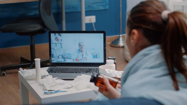 Patient with flu using video call communication for healthcare consultation with doctor. Ill woman holding bottle of pills and tablet with capsules for treatment advice and medication.