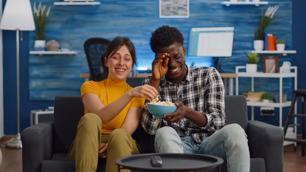 Cheerful interracial couple laughing at comedy on television