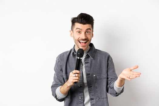 Handsome smiling performer talking in mic, gesturing and performing, making speech with microphone, standing against white background