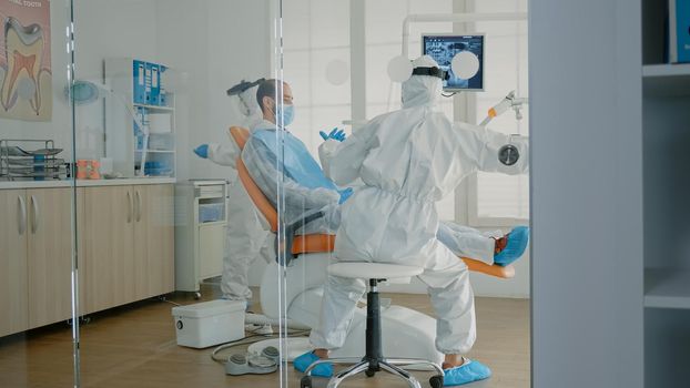 Orthodontists and patient wearing ppe suits in oral cabinet