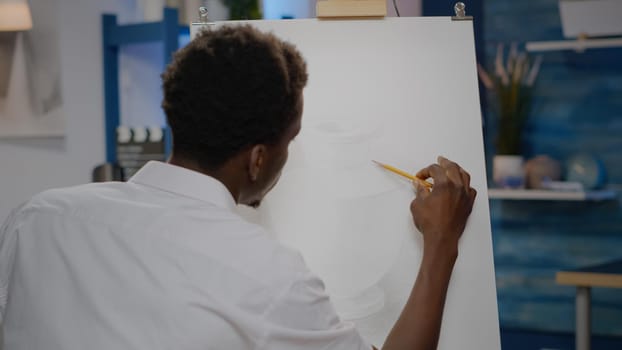 Young black artist using art pencil on canvas for vase drawing