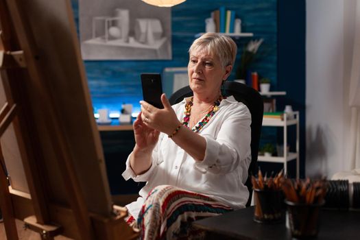 Senior artist using smartphone sitting in art studio room