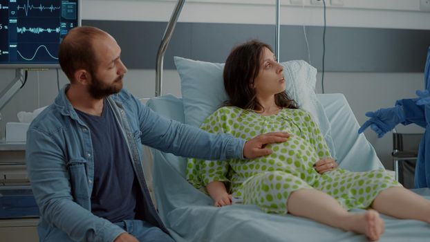Young woman with baby bump sitting in hospital ward bed