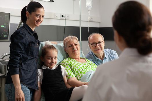Physician doctor checking sick senior woman discussing healthcare treatment during clincal therapy. Caring cheerful family visiting retired elderly patient in hospital ward. Medical recovey