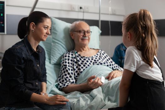 Elderly sick old man resting in bed talking with caring granddaughte