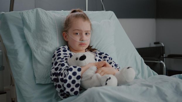 Portrait of little girl patient wearing oxygen nasal tube resting in bed recovery