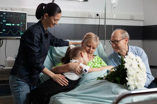 Caring granddaughter hugging sick grandmother while visiting her in hospital ward