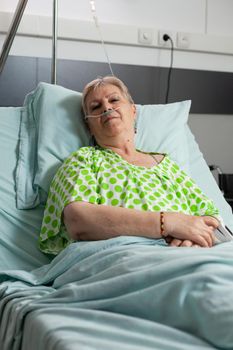 Portrait of sick pensioner woman looking into camera while resting in bed