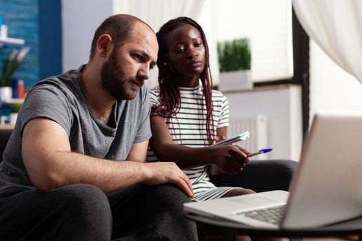 Interracial couple using laptop for taxes payment and economy