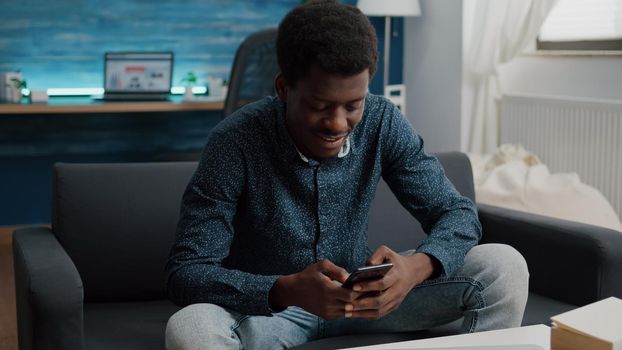 Black guy in his living room using phone to browse social media