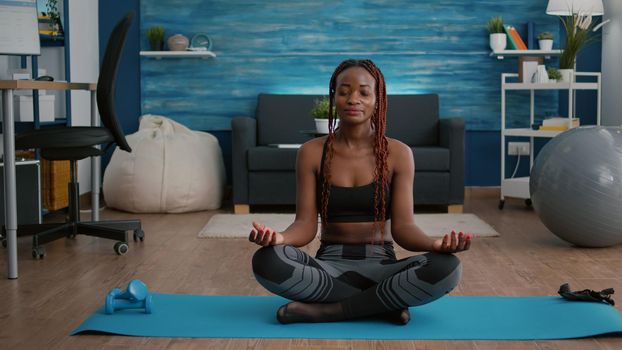 Portrait of black woman sitting in lotus position on floor doing morning breathing workout
