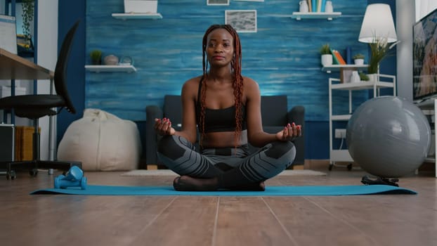 Athlete slim woman with dark skin putting in lotus position on yoga map