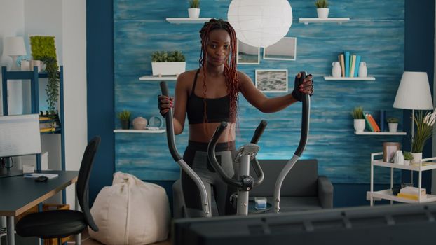 Black woman athletic training on elliptical bike practicing cardio sport