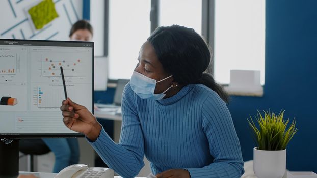 African employee with face mask explaning project to invalid coworker