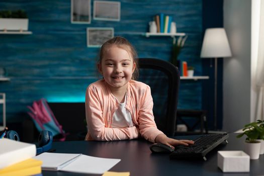 Portrait of smiling little schoolchild sitting at desk table in living room