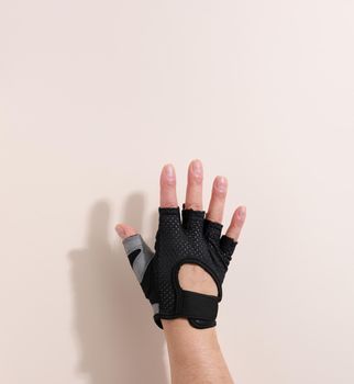 black sports glove on a female hand, beige background. Part of the body is lifted up