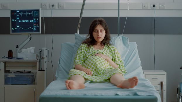 Portrait of pregnant person sitting in hospital ward bed