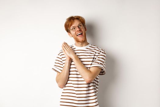 Happy redhead man clap hands and looking satisfied at upper right corner, getting ready for something, standing over white background
