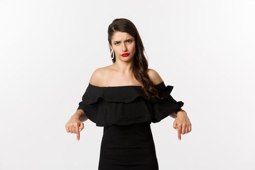 Fashion and beauty. Displeased woman complaining, frowning and pointing fingers down at bad thing, express disappointment and dislike, white background