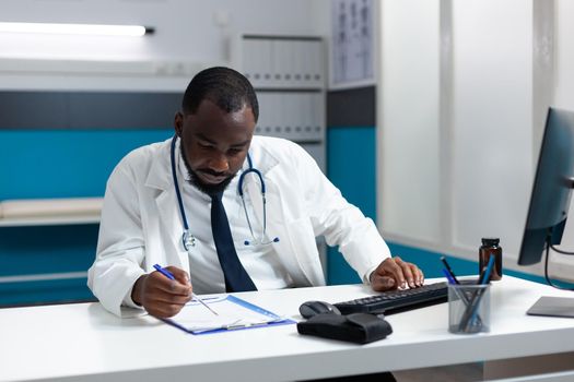 African american physician doctor typing healthcare treatment on computer after analyzing disease symptoms expertise during medical consulation. Therapist working in hospital office
