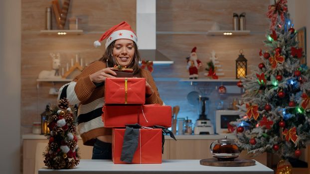 Woman with santa hat carrying gifts in decorated kitchen