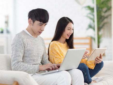 Young couple using laptop for office and watching movies on sofa at home