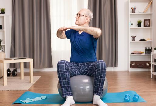 Granddad practicing sport at home for a healty life. Old person pensioner online internet exercise training at home sport activity with dumbbell, resistance band, swiss ball at elderly retirement age.