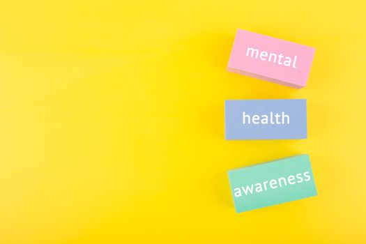 Mental health awareness written on colorful rectangles on yellow background with copy space