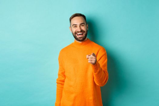 Handsome man laughing and pointing at camera, nodding in approval, agree with you, standing over light blue background